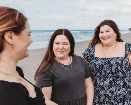 3 friends on the beach in New Zealand wearing long necklace stacks, earrings, and bracelets