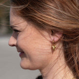 Woman wearing Chic Heart Huggies in gold with sleek heart-shaped hoops, also offered in silver
