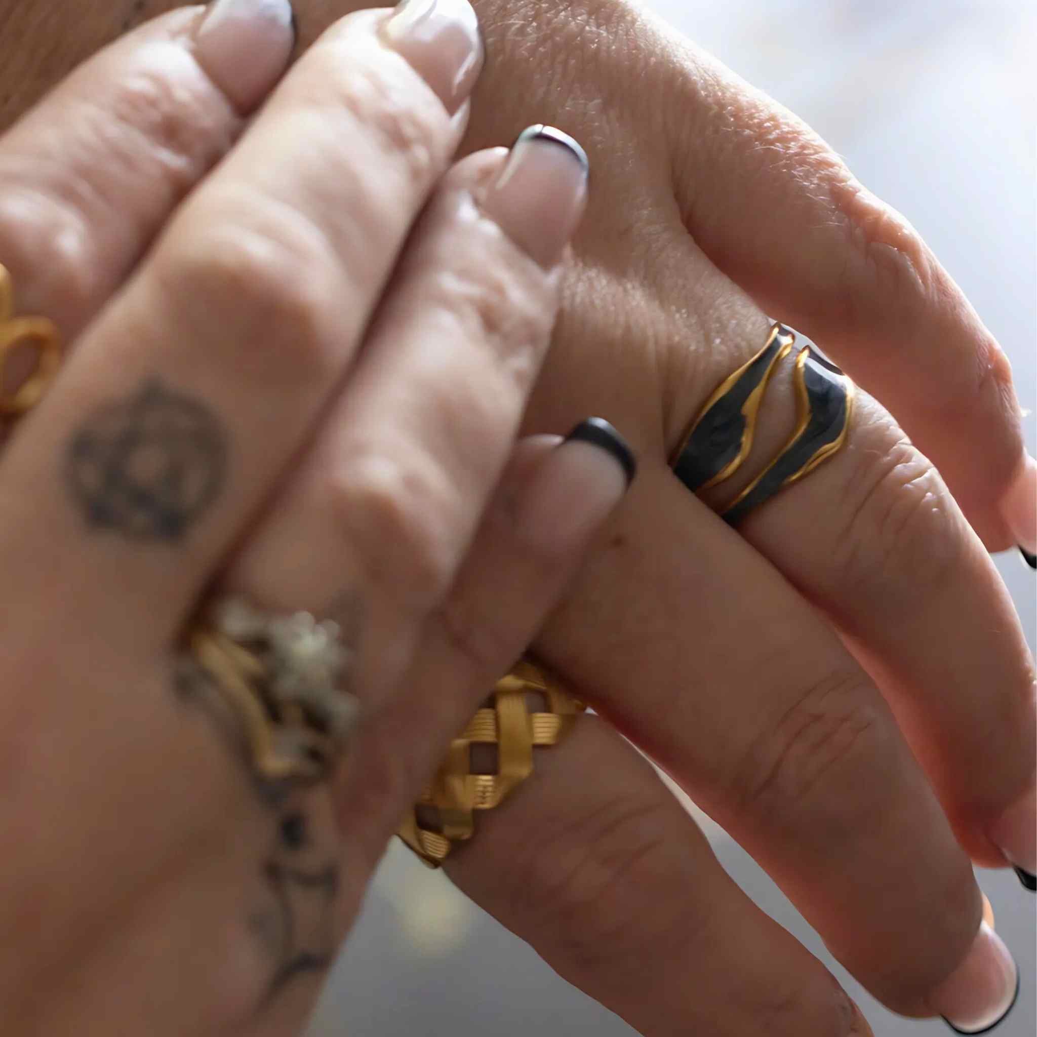 Woman wearing the Flowing Waters adjustable ring in gold with black enamel accent and fluid, wave-like design