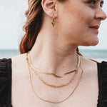 Model showcasing a stacked look with three gold-plated necklaces: Snake Chain, Paperclip Chain, and Delicate Twist Chain. Elegant and versatile, perfect for layering.