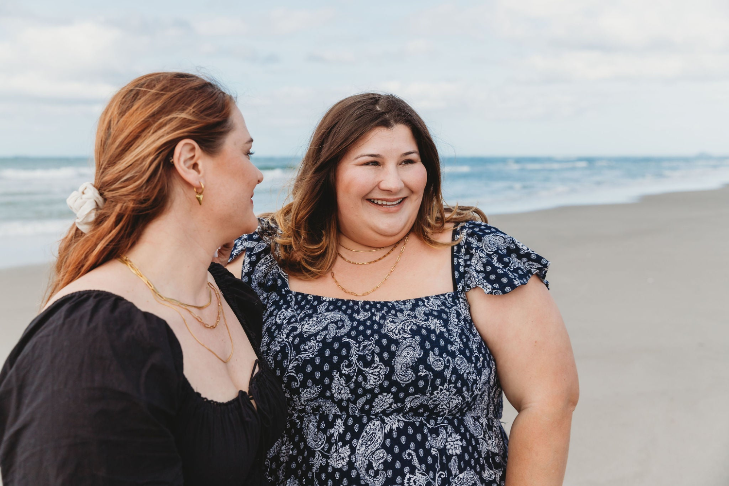 Wendy + Kathryn on the beach wearing necklace stacks in gold